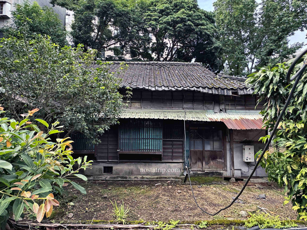 青田街木造老宅正面，屋瓦斑駁，前院雜草叢生