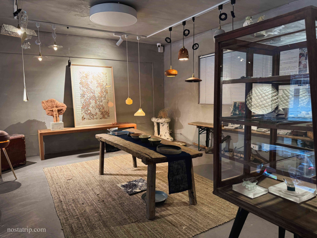 一嶼 Island 展示空間角落，一張老木桌搭配懸吊燈飾與藝術擺件，營造靜謐的展覽氛圍