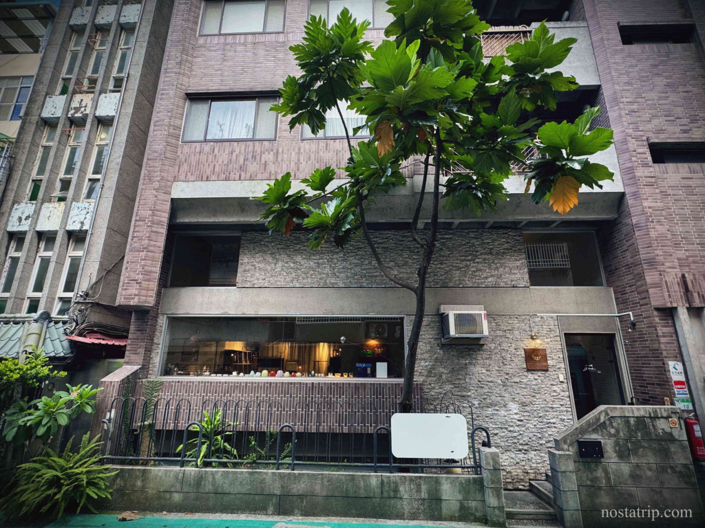 一嶼 Island 外觀建築，石牆搭配大片玻璃窗，前景綠植與樹木點綴巷弄街景