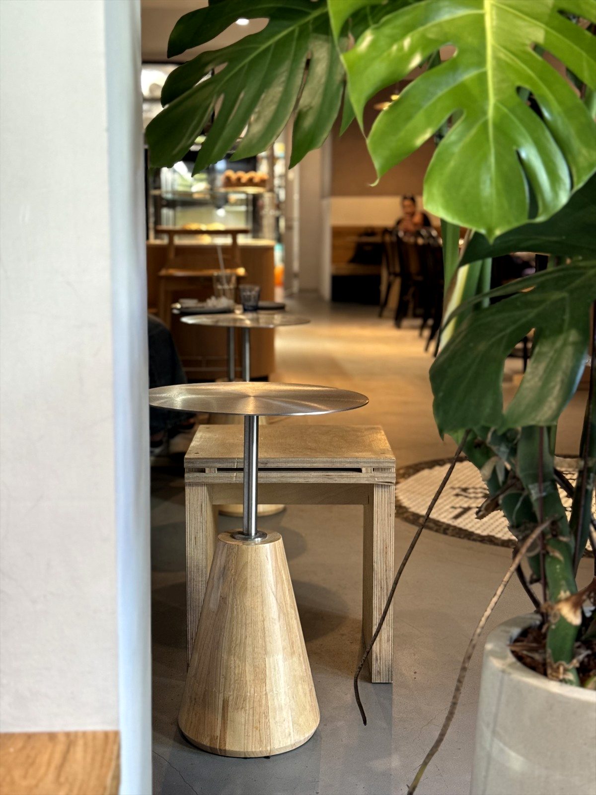 Supranormal Bakery Café 白牆旁的木桌、綠色植栽與室內座位