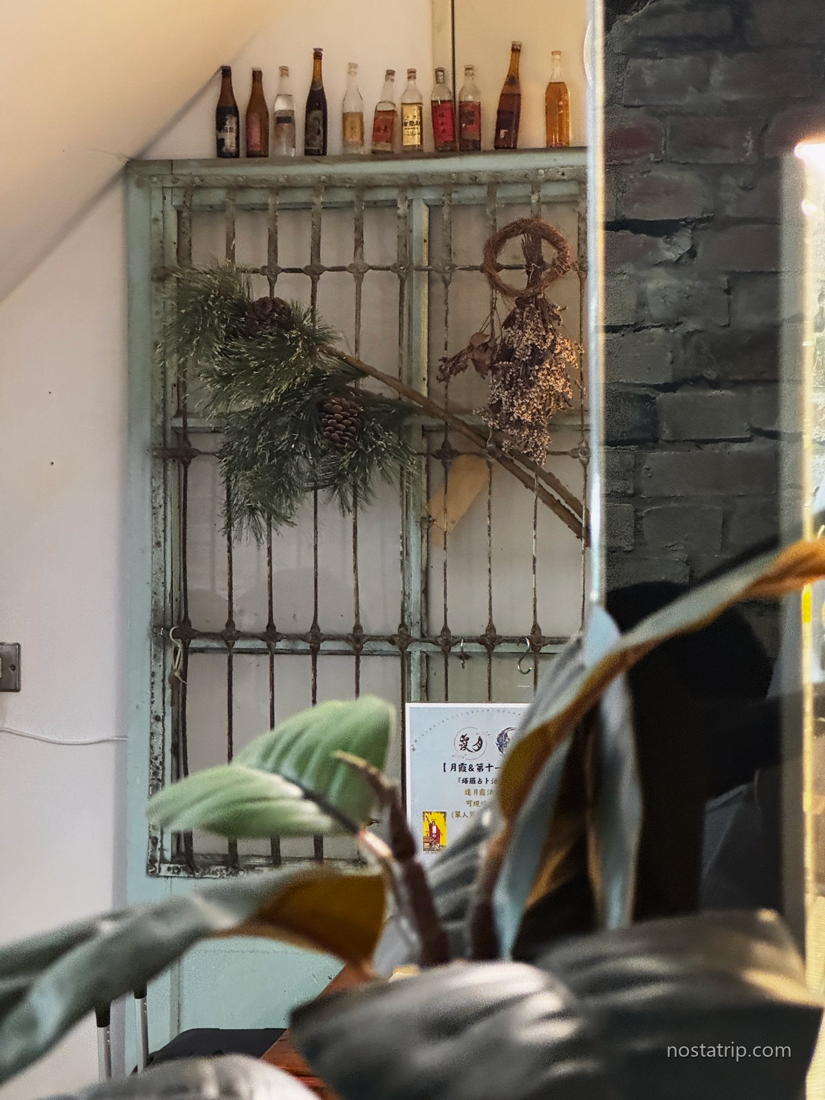 月霞 Waha Cafe 店內斑駁的淺藍色鐵欄舊門,掛著綠植與乾燥花,上方排列玻璃瓶
