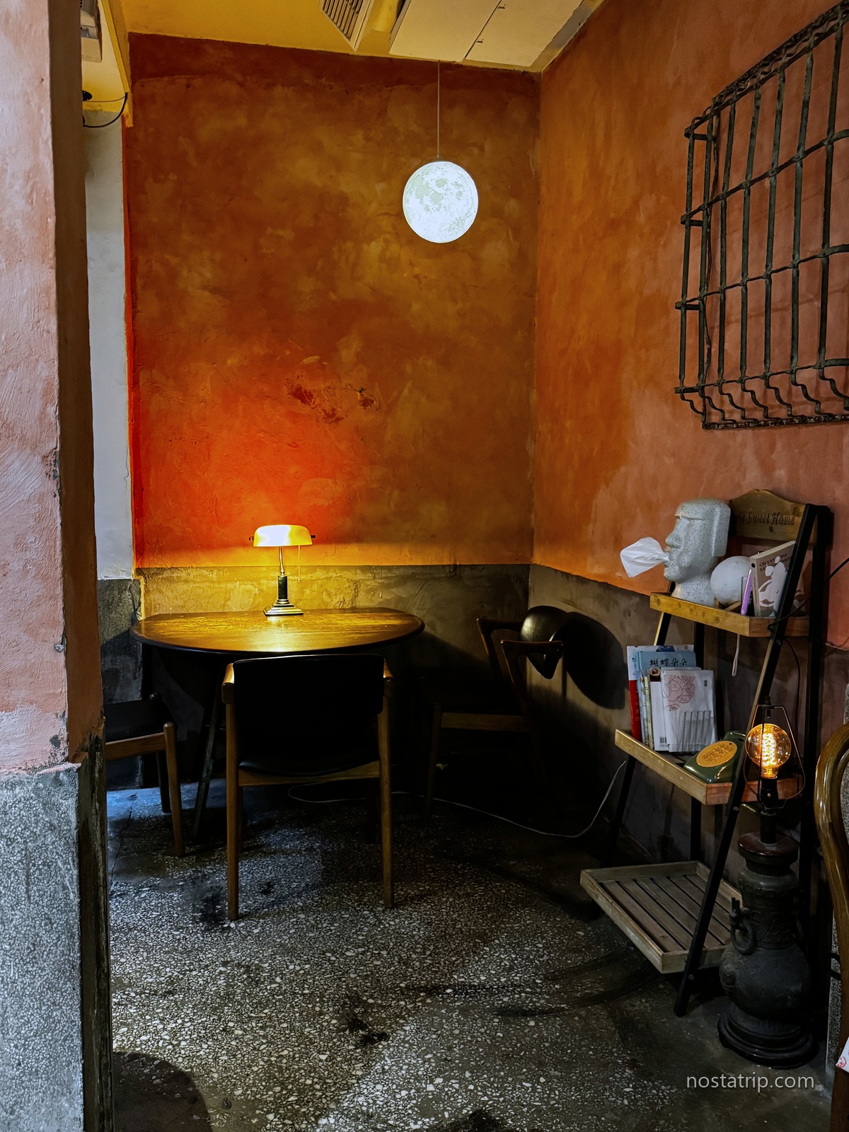 赤峰街月霞 Waha Cafe 的座位角落,圓木桌、綠色桌燈與深色木椅映著紅褐色牆面