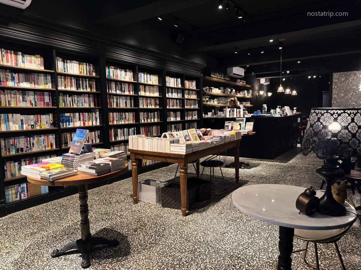 赤峰街春秋書店室內，整面黑色書架前擺放木質書桌，後方設有咖啡吧台，地面為磨石子。