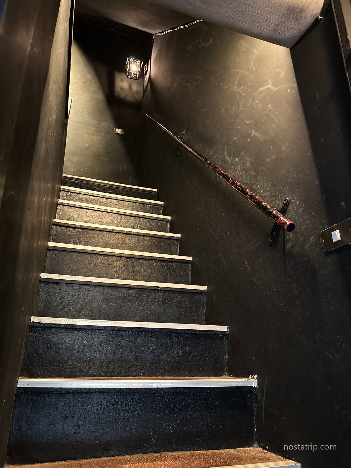 春秋書店通往樓上的深色階梯，金屬扶手沿牆延伸，暖色壁燈照亮牆面與階緣。