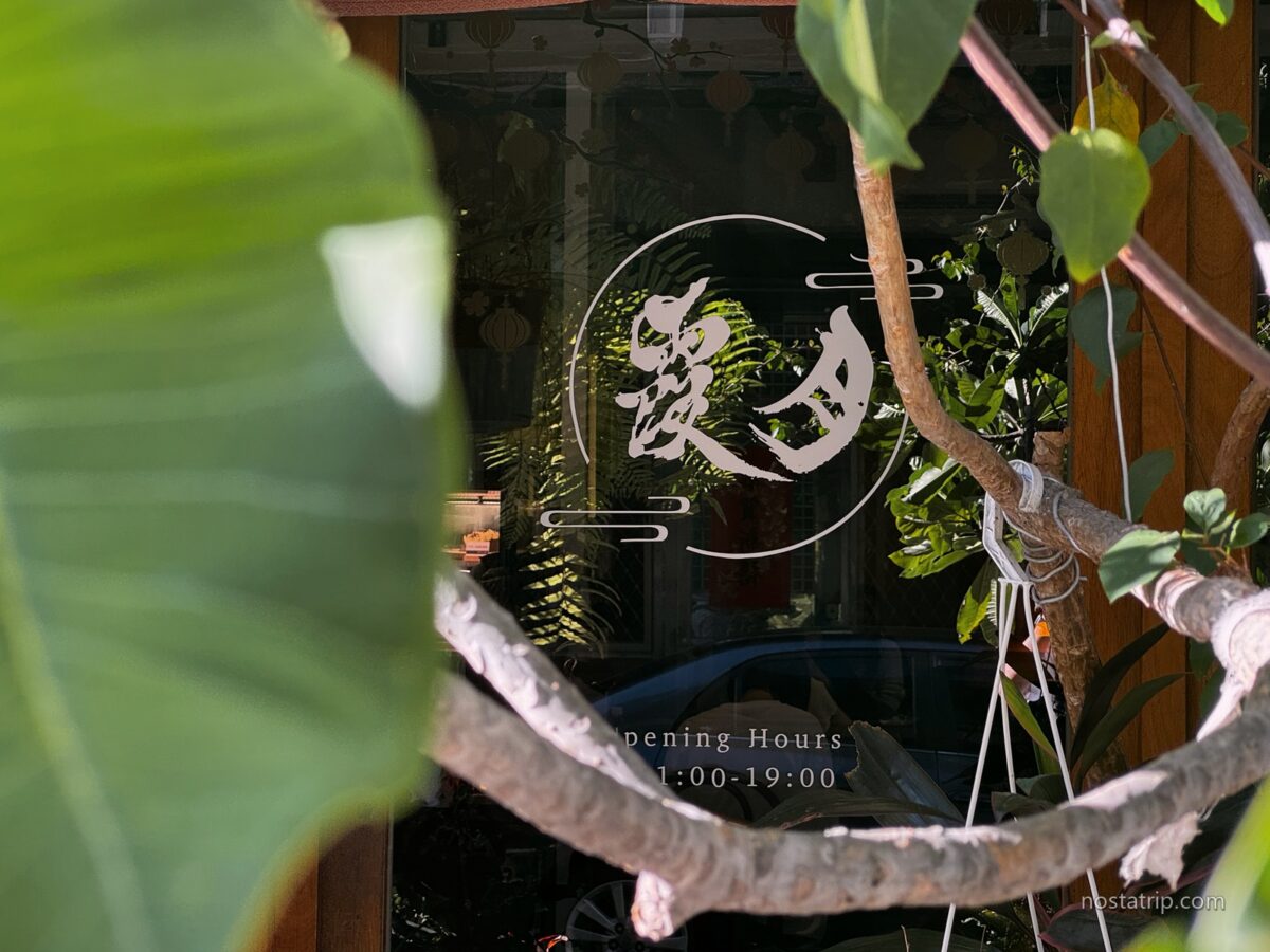 赤峰街月霞 Waha Cafe 玻璃門上的白色店名字樣,前景被綠色葉片與枝幹遮映